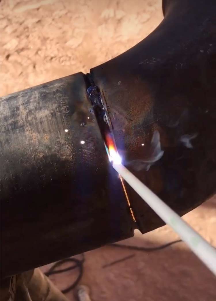 Close-up action shot of a skilled welder performing a root pass repair on a carbon steel tubing joint, joining two sections with an active arc and precise electrode control