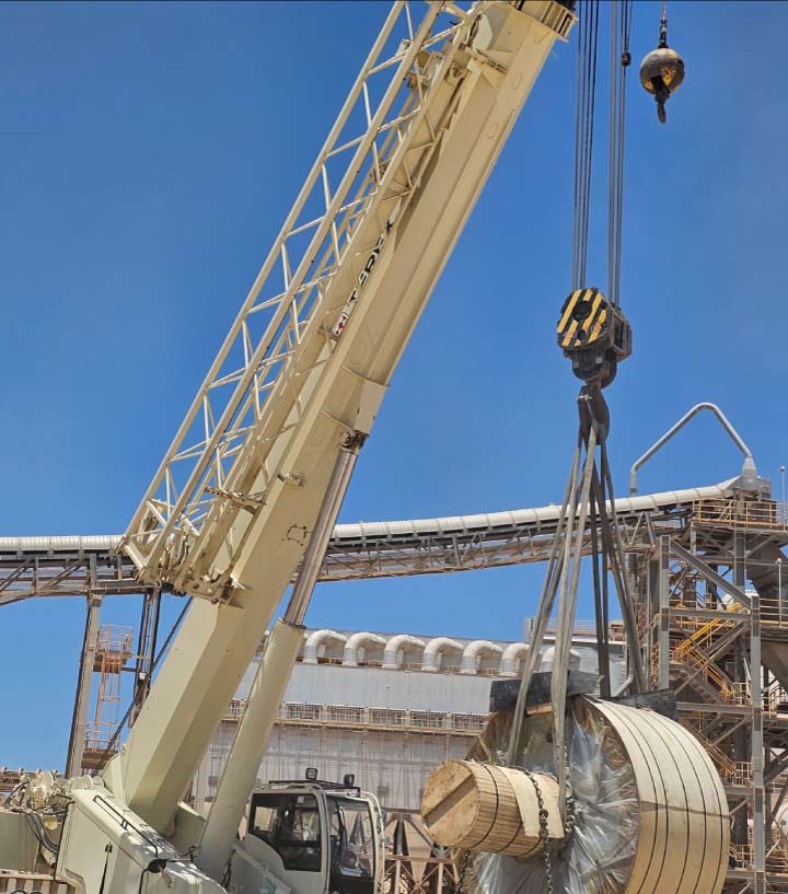 A heavy-duty white industrial crane at a processing plant lifting a large cylindrical metal component during a scheduled facility turnaround and equipment upgrade.