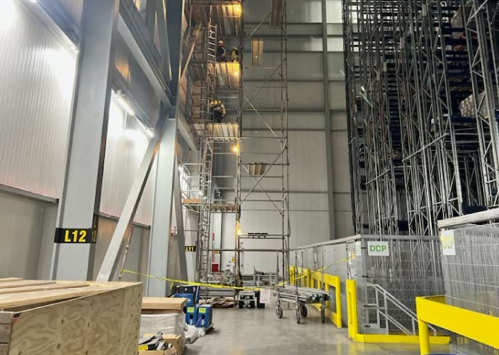 View of an expansive industrial facility with tall vertical steel columns and multi-level scaffolding erected for high-altitude metal fabrication and building maintenance.