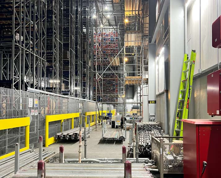 High-density industrial storage facility showing vertical steel support beams, metal shelving units, and yellow safety guardrails requiring regular structural integrity inspections.