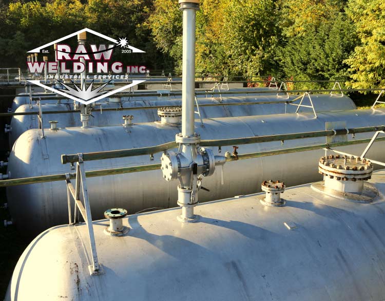 A row of silver industrial storage pressure vessels at an outdoor facility with the RAW Welding Inc. brand logo superimposed