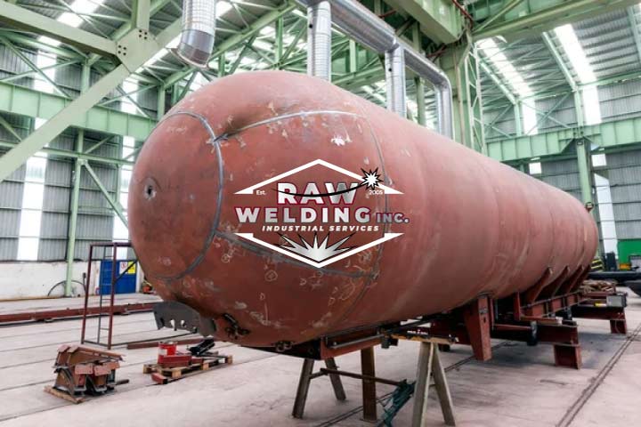 A large, horizontal red-primed pressure vessel in an industrial warehouse featuring the RAW Welding Inc. company logo.